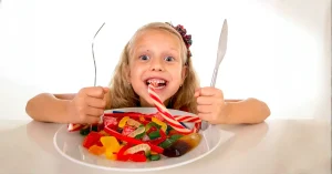 ילדה אוכלת צלחת מלאה ממתקים עם מזלג וסכין