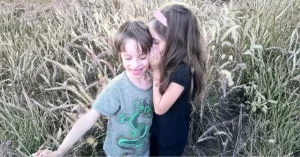 שני ילדים בשדה, ילדה לוחשת סוד באוזן אחיה, אווירה חמה של קרבה וסודיות